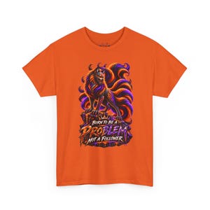 May include: An orange short-sleeve t-shirt featuring a graphic of a multi-tailed fox with purple and orange fur standing on a rock. Below the fox, the text reads BORN TO BE A PROBLEM NOT A FOLLOWER in stylized orange and purple lettering.