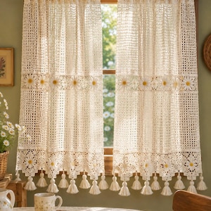 May include: A pair of off-white crochet curtains featuring a grid pattern, horizontal bands of daisy motifs with yellow centers, and a bottom edge finished with decorative tassels. The curtains are hung on a dark brown rod over a window frame.