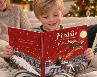 Puede incluir: Un libro infantil de tapa dura titulado Freddie and the Little Reindeer's First Flight con una cubierta roja que muestra un reno volador, un niño, un pueblo nevado y estrellas doradas. El texto dice A little courage. A little kindness. A magical Christmas flight.