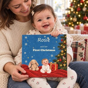 A smiling mother holds her baby beside a Christmas tree with a personalised Baby's First Christmas book reading Rosie and her First Christmas on a blue cover. Rosie is an example name.