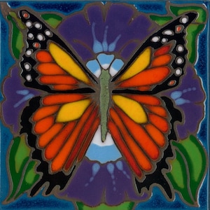 May include: A colorful ceramic tile with a butterfly design. The butterfly has black wings with orange, red, and yellow accents. The butterfly is centered on a purple flower with green leaves.