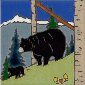 May include: A ceramic tile with a black bear and a cub walking on a green hill. The background features a blue sky, white snow-capped mountains, and a brown branch. There are green trees and a birch tree with a white trunk.