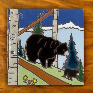 May include: A square ceramic tile featuring a hand-painted scene of a large black bear and a smaller cub in a forest. The design includes white birch trees, green grass, a brown path, dark blue evergreen trees, and distant white mountains.