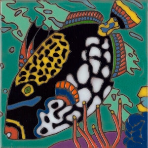 May include: A colorful ceramic tile featuring a black and white pufferfish with yellow and orange accents swimming in turquoise water. The fish is surrounded by coral and seaweed.
