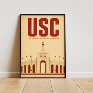 May include: A framed poster featuring a graphic illustration of the Los Angeles Memorial Coliseum in red and cream tones. The text USC appears in large red letters at the top, with Los Angeles Memorial Coliseum and Los Angeles, California below.