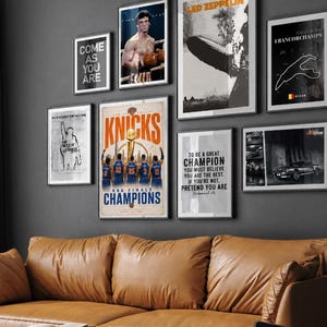 Pode incluir: Uma parede de galeria com oito cartazes emoldurados com temas diversos, incluindo um campeonato de basquete, uma luta de boxe, uma banda de rock, um mapa de circuito de corrida, um carro cl&aacute;ssico e cita&ccedil;&otilde;es motivacionais em texto preto e branco.