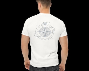 Puede incluir: Una camiseta blanca de manga corta con un gráfico azul oscuro en la espalda. El diseño muestra una rosa de los vientos rodeada de anillos orbitales y una estrella, con el texto "THINK CELESTIAL" impreso en un arco bajo la brújula.