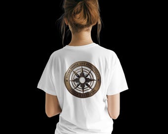 Puede incluir: Una camiseta blanca de manga corta con un gráfico circular en la espalda. El diseño incluye un emblema de estrella de brújula en tonos bronce rodeado por el texto "THINK DEEPLY. LIVE BEAUTIFULLY. THINK CELESTIAL" impreso en un borde circular oscuro.
