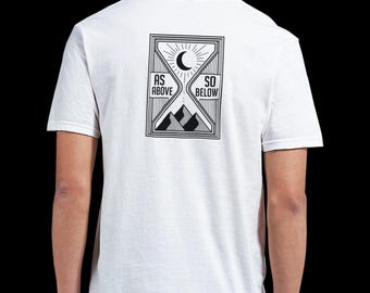 Puede incluir: Una camiseta blanca de manga corta con un gráfico negro en la parte posterior. El diseño tiene forma de reloj de arena con una luna creciente y rayos de sol en la parte superior, montañas en la inferior y el texto AS ABOVE SO BELOW a los lados.
