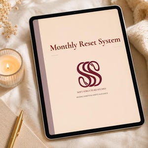 May include: A digital tablet displaying a document titled Monthly Reset System with a dark red logo for Soft Structure Studio and the text Where Ambition Meets Elegance on a light beige background, featuring a dark border and a thin purple side stripe.