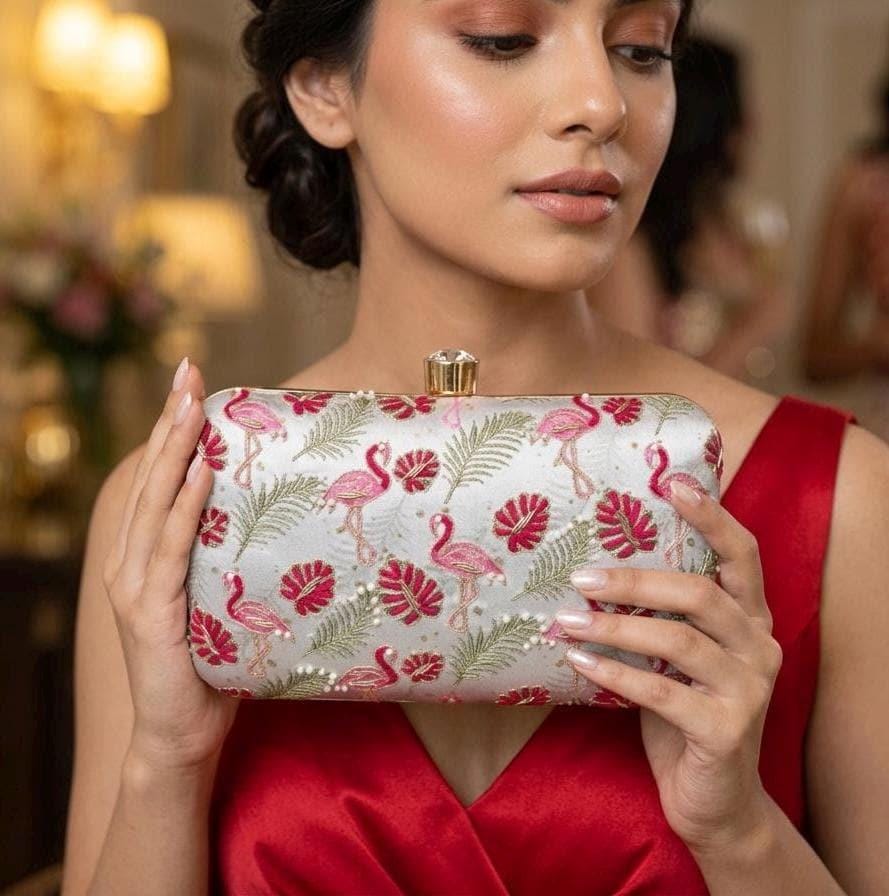 Model in a red dress holding the flamingo palm print embroidered clutch