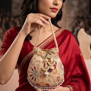 May include: A beige drawstring handbag featuring intricate multi-colored floral embroidery, gold-toned thread accents, and a dangling pearl-beaded fringe along the bottom edge. The bag includes a pearl-embellished handle and decorative tassels.