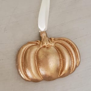 May include: A gold-colored ceramic pumpkin ornament with a white ribbon for hanging.