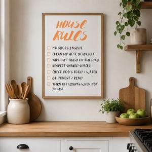 Può includere: Un cartello da parete incorniciato con bordo in legno chiaro che presenta il testo arancione HOUSE RULES. Sotto ci sono sette caselle di controllo con testo nero: NO SHOES INSIDE, CLEAN UP AFTE YOURSELF, TAKE OUT TRASH ON TUESDAY, RESPECT SHARED SPACES, CHECK DOG'S FOOD / WATER, BE HONEST / KIND, TURN OFF LIGHTS WHEN NOT IN USE.