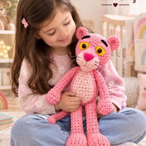 Puede incluir: Un peluche hecho a mano de ganchillo del personaje de la Pantera Rosa. La figura está confeccionada con hilo rosa brillante con una barriga de color rosa más claro, ojos amarillos con pupilas negras, cejas negras y una nariz rosa oscuro con bigotes de hilo negro.