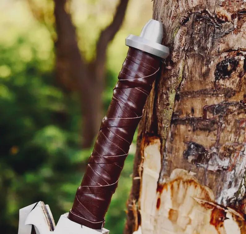 May include: A cylindrical handle wrapped in dark brown leather strips with a silver-colored metal pommel at the top. The handle features a spiral pattern created by the overlapping leather wrap, ending in a metallic cap with a rounded top.