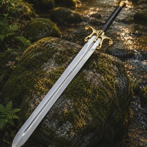 May include: A double-edged steel sword featuring a polished silver blade with a central fuller. The hilt includes a gold-colored metal crossguard with ornate, curved scrollwork details and a black leather-wrapped grip with a flared pommel.