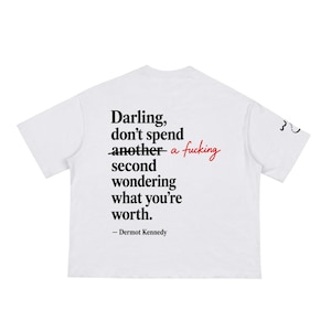 Peut inclure: Un t-shirt blanc à manches courtes avec le texte noir suivant : Darling, don't spend another a fucking second wondering what you're worth. — Dermot Kennedy. Le mot another est barré d'un trait noir et un petit motif figure sur la manche.