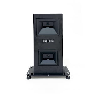 May include: A black rectangular electronic device with two recessed camera lenses stacked vertically. The word UNEEKOR is printed in white text in the center of the unit. The device is mounted on a flat black base with four small feet.