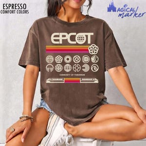 Puede incluir: Una camiseta marrón de manga corta con el texto EPCOT y COMMUNITY OF TOMORROW en blanco. El gráfico incluye rayas horizontales en amarillo, naranja y rojo, junto con una cuadrícula de varios iconos circulares y una ilustración de un monorraíl.