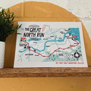 Könnte beinhalten: Ein rechteckiger Druck mit einer Karte der Strecke des Great North Run 2026. Die Karte zeigt den Weg von Newcastle Upon Tyne nach South Shields, einschließlich des Flusses Tyne, verschiedener Wahrzeichen, einer Windrose und dem Text My First Half Marathon 2hrs 22.