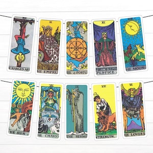 Può includere: Una ghirlanda decorativa con dieci carte dei tarocchi appese a due cordini neri. Le carte mostrano illustrazioni colorate dell'Appeso, dell'Imperatrice, della Ruota della Fortuna, della Giustizia, della Luna, del Sole, del Carro, dell'Eremita, della Forza e degli Amanti.