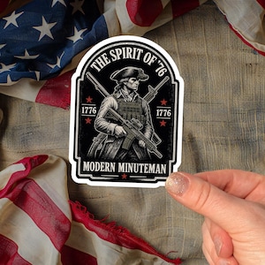 May include: A die-cut sticker featuring a black and white illustration of a soldier in a tricorn hat and tactical gear holding a rifle. The text reads THE SPIRIT OF '76, 1776, and MODERN MINUTEMAN. The design includes red stars and crossed rifles.