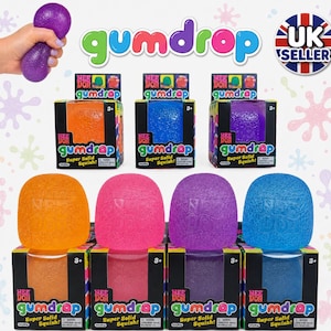 Puede incluir: Una colección de juguetes blandos Nee Doh Gumdrop en naranja, rosa, morado y azul. Cada juguete viene en una caja negra con el texto Nee Doh gumdrop Super Solid Squish. Los juguetes tienen una superficie texturizada y translúcida.