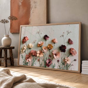 May include: A rectangular framed wall art piece featuring a textured impasto painting of various wildflowers in shades of dusty pink, deep burgundy, cream, and muted orange against a pale sage green background, set in a light wood frame.