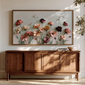 May include: A rectangular wall art piece featuring an oil painting of various flowers in shades of pink, orange, red, and cream against a textured off-white background, framed in a thin wooden border and displayed above a wooden sideboard.