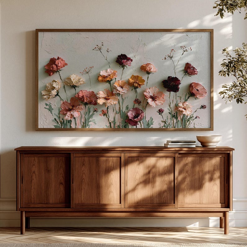 May include: A rectangular wall art piece featuring an oil painting of various flowers in shades of pink, orange, red, and cream against a textured off-white background, framed in a thin wooden border and displayed above a wooden sideboard.