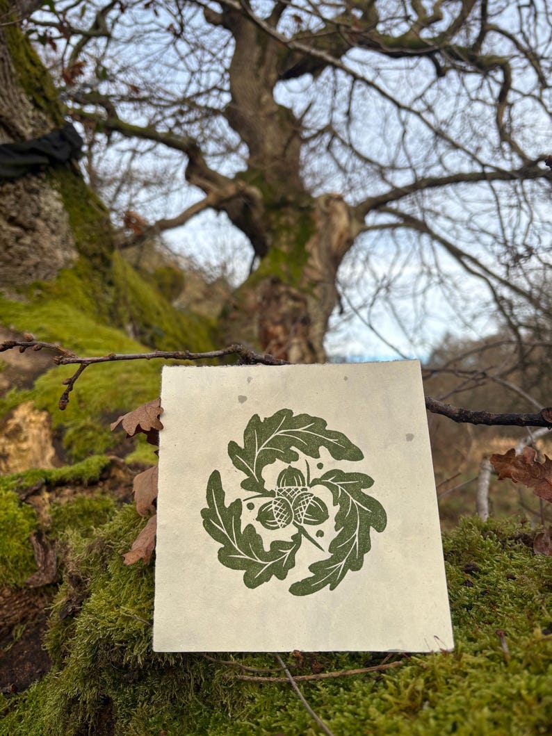 Pode incluir: Uma impress&atilde;o verde e branca de uma coroa de folhas de carvalho com tr&ecirc;s bolotas no centro. A impress&atilde;o est&aacute; em um peda&ccedil;o de papel com uma textura &aacute;spera.