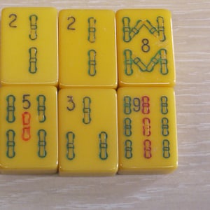 May include: Six rectangular yellow mahjong tiles arranged in two rows of three. The tiles feature engraved bamboo suit markings in green and red, along with black numerical characters including 2, 8, 5, 3, and 9, representing various game values.