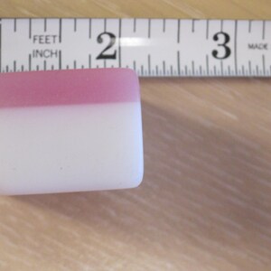 May include: A rectangular, two-tone object with a pink top and white bottom, next to a ruler. The ruler is marked in inches and reads "MADE IN U.S.A."