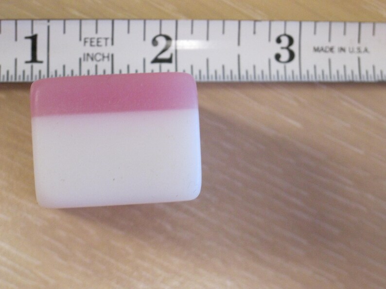 May include: A rectangular, two-tone object with a pink top and white bottom, next to a ruler. The ruler is marked in inches and reads "MADE IN U.S.A."