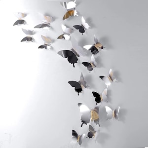 May include: A collection of multiple butterfly-shaped wall decals in varying sizes. Each butterfly features a reflective, mirror-like silver finish with a central gold-toned accent along the body, arranged in a scattered, upward-flowing pattern.