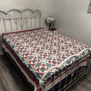 Könnte beinhalten: Eine rechteckige Steppdecke mit einem sich wiederholenden geometrischen Muster in den Farben Dunkelrot, Dunkelgrün und Creme. Der Stoff zeigt komplexe Blumen- und Kleinmuster sowie eine dekorative Bordüre an den Rändern der Tagesdecke.