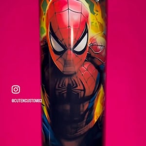 May include: A cylindrical tumbler featuring a vibrant, full-wrap graphic of the superhero Spider-Man in his iconic red and blue suit. The design includes yellow and orange flame-like accents, a black spider emblem on the chest, and a clear lid.