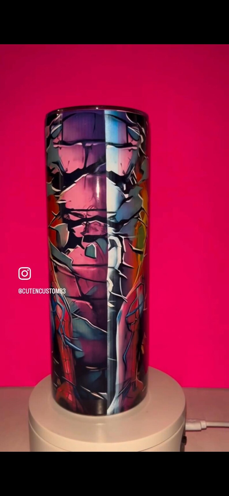 May include: A cylindrical tumbler featuring a vibrant graphic design with a cracked, shattered effect. The artwork displays a split color palette of deep purples, blues, and reds, incorporating comic book style imagery and the text CUTENCUSTOM83.