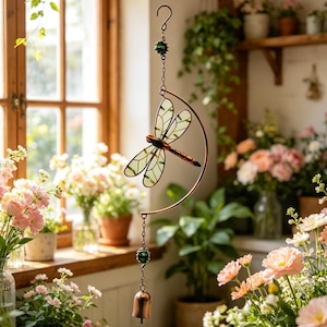 May include: A hanging dragonfly ornament featuring light green stained glass wings and a copper-toned body. The dragonfly is attached to a curved copper wire frame, accented with green glass beads and a small copper bell at the bottom end.