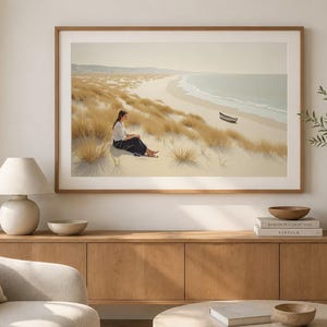 May include: A framed landscape wall art print depicting a serene coastal scene with golden sand dunes, tall grasses, and a calm ocean. A small boat rests on the shoreline, while a figure sits quietly amidst the dunes under a soft, hazy sky.