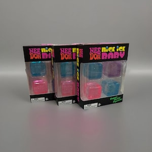 Puede incluir: Tres cajas rectangulares de juguetes sensoriales Nee Doh Nice Ice Baby. Cada caja negra presenta texto en rosa y amarillo y contiene cuatro juguetes blandos translúcidos en forma de cubo en colores azul, morado y rosa. El empaque incluye el texto Super Solid Squish.
