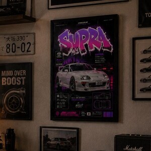 May include: A living room wall decorated with automotive-themed posters, including a central print of a white Toyota Supra with purple neon text, a TRD banner, Japanese license plates, and framed car illustrations above a wooden media console.