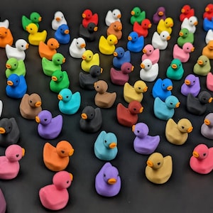 May include: A large collection of miniature rubber ducks in a wide variety of solid colors including red, orange, yellow, green, blue, purple, pink, white, black, and brown. Each small duck features a distinct orange beak and black eyes.