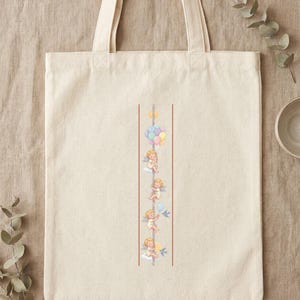Pode incluir: Uma sacola de lona na cor creme com um design gr&aacute;fico vertical. A ilustra&ccedil;&atilde;o retrata quatro pequenos querubins com asas, cada um segurando um poste central, acompanhados por bal&otilde;es em tons pastel e pequenos p&aacute;ssaros azuis em voo.
