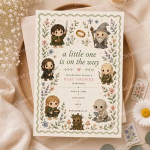 May include: A baby shower invitation with a whimsical design featuring characters from a fantasy story. The invitation has a floral border and includes the text "a little one is on the way". The invitation is on a cream-colored background.