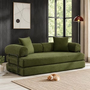 May include: A low-profile olive green corduroy sofa bed featuring a structured black metal frame on the sides, two matching square throw pillows, and a thick, rectangular seat cushion. The design includes rounded armrests and a clean, linear aesthetic.