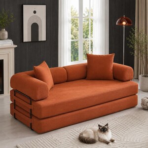 May include: A rust-orange corduroy sofa bed featuring a low-profile design with a black metal frame, two cylindrical side bolsters, and one square back cushion. The textured fabric covers the entire seating area and the integrated armrests.
