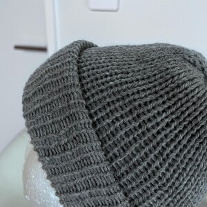 May include: A dark grey knit beanie with a thick folded cuff. The hat is constructed from a ribbed yarn texture, featuring a consistent vertical stitch pattern throughout the crown and the brim, creating a simple and functional headwear piece.