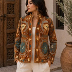 Può includere: Una giacca a maniche lunghe aperta sul davanti, realizzata in tessuto di velluto color arancio bruciato. Il capo presenta un intricato ricamo floreale multicolore nei toni del verde ottanio, crema e oro, con collo alla coreana e orlo dritto.